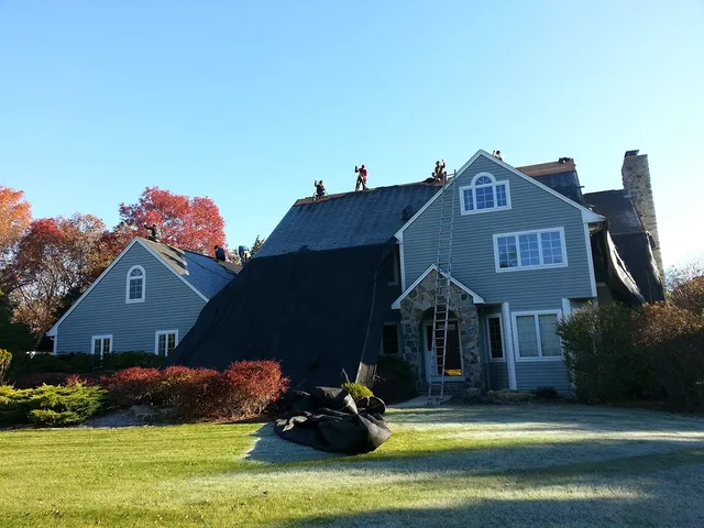 Gray home with the old roof stripped and covered in tarps