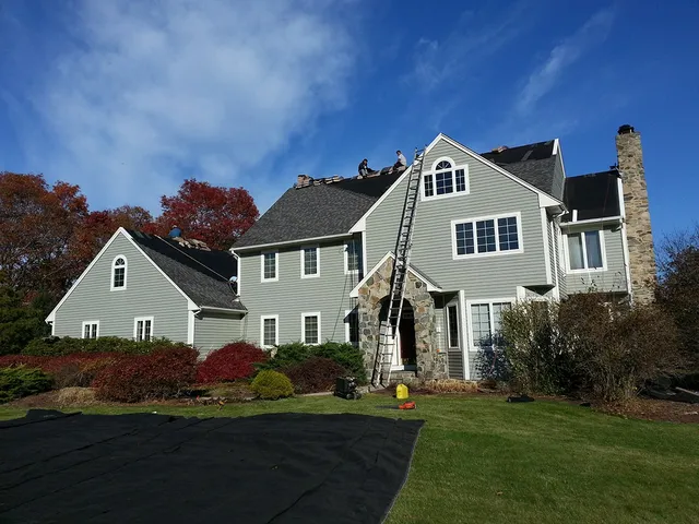 Crew and ladder on a gray colonial during a roof replacement